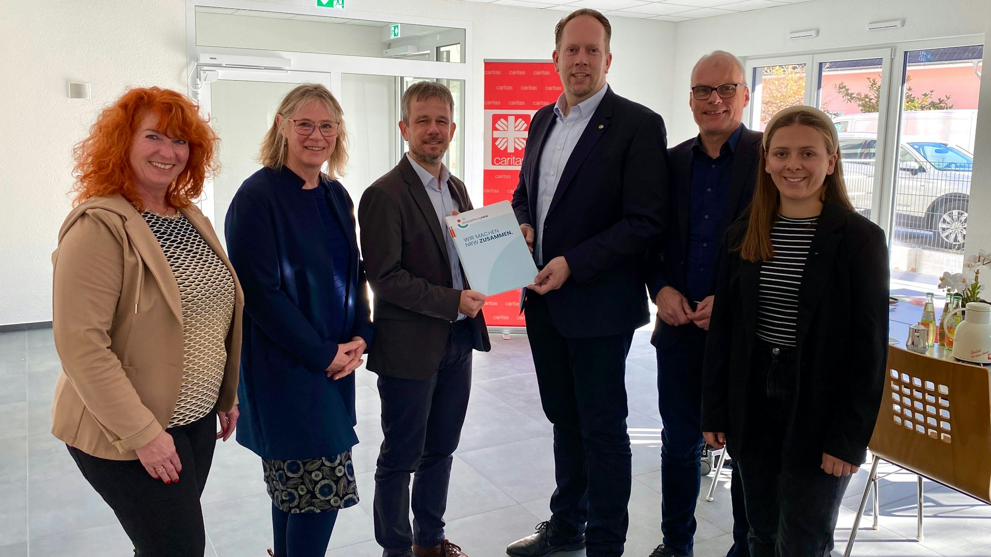 Sechs Menschen stehen in einem großen, leeren Raum.