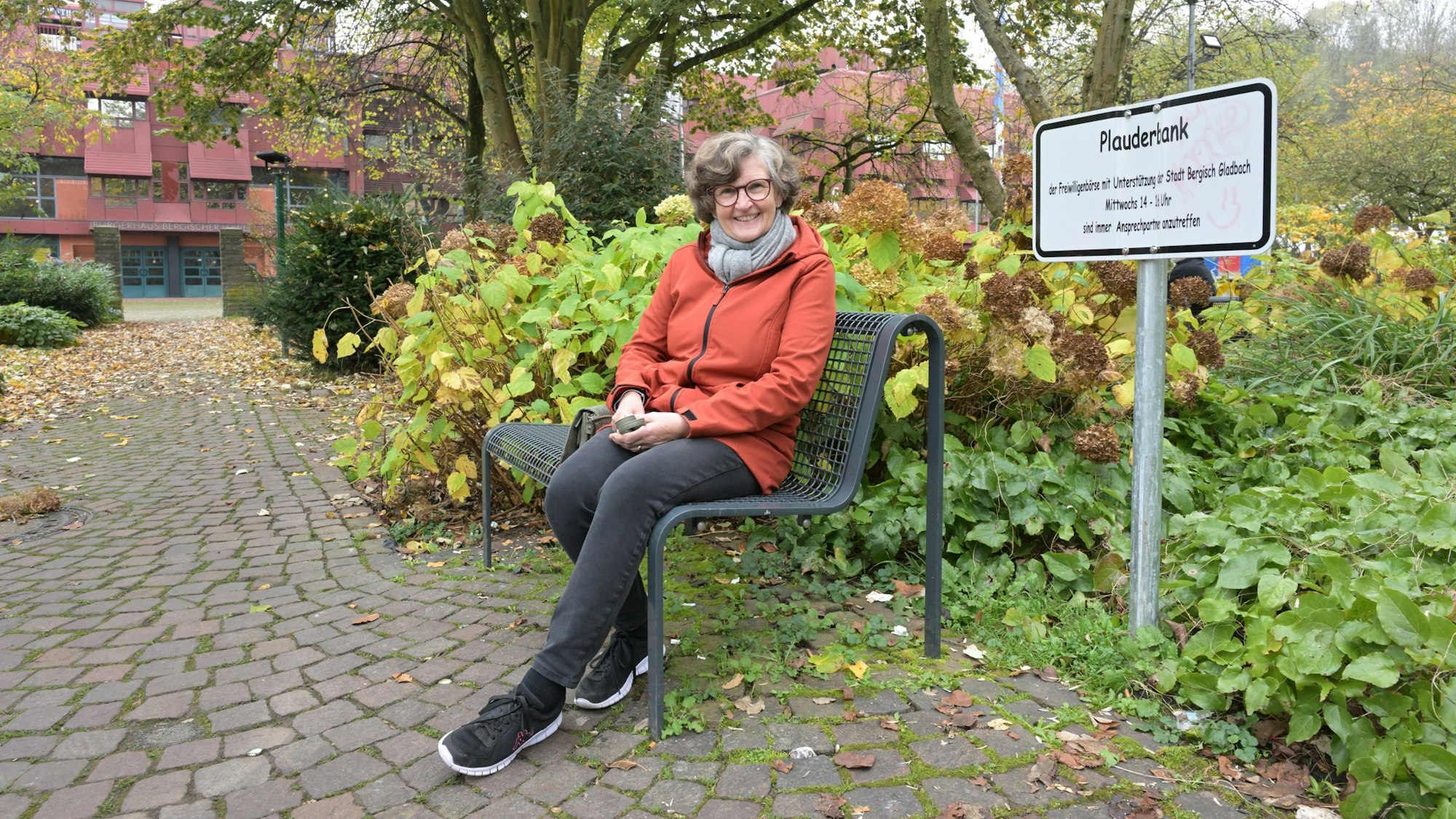 Annette Kruff sitzt auf der Bank. Daneben steht ein Schild mit der Aufschrift Plauderbank.