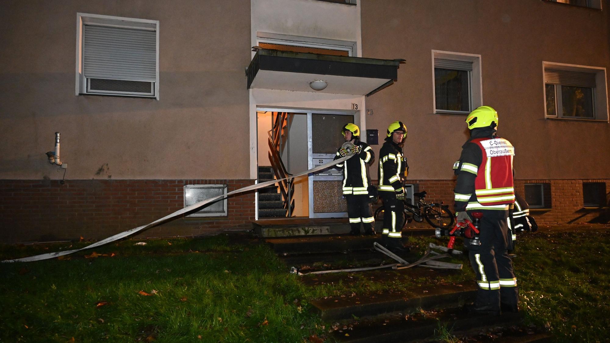 Drei Feuerwehrleute stehen vor dem Eingang eines Wohnhauses. Einer von ihnen rollt einen Löschwasserschlauch auf.