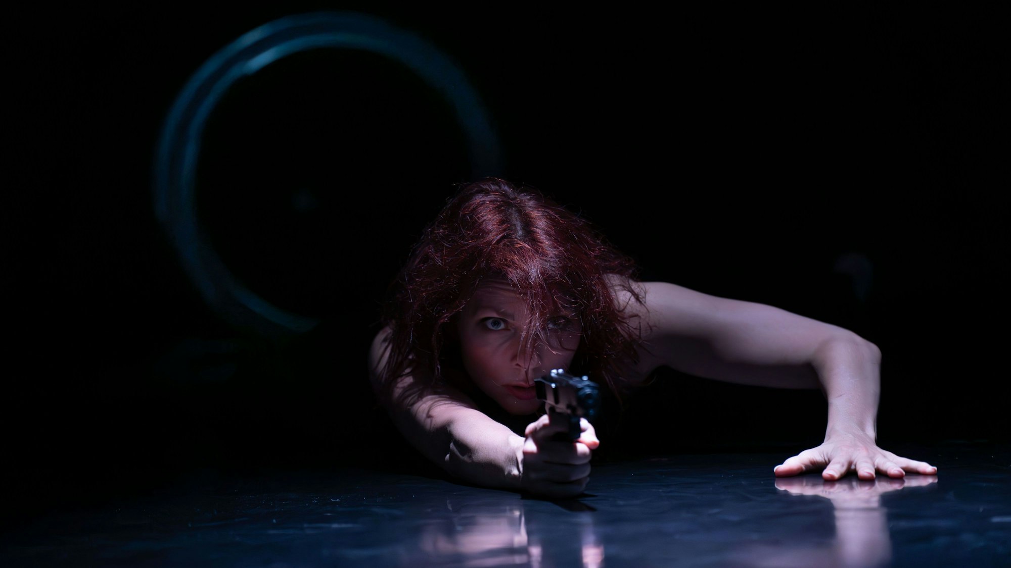 Eine Frau liegt mit ausgestreckter Hand auf dem Boden und zielt mit einer Pistole.