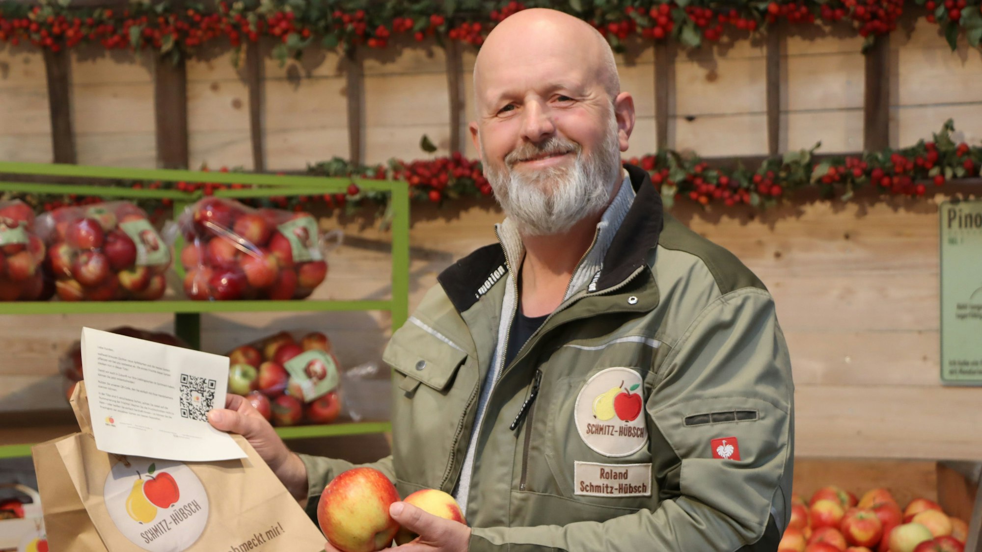 Auf dem Bild ist ein Apfelzüchter zu sehen. Hinter ihm stehen Regale mit Tüten voller Äpfel.