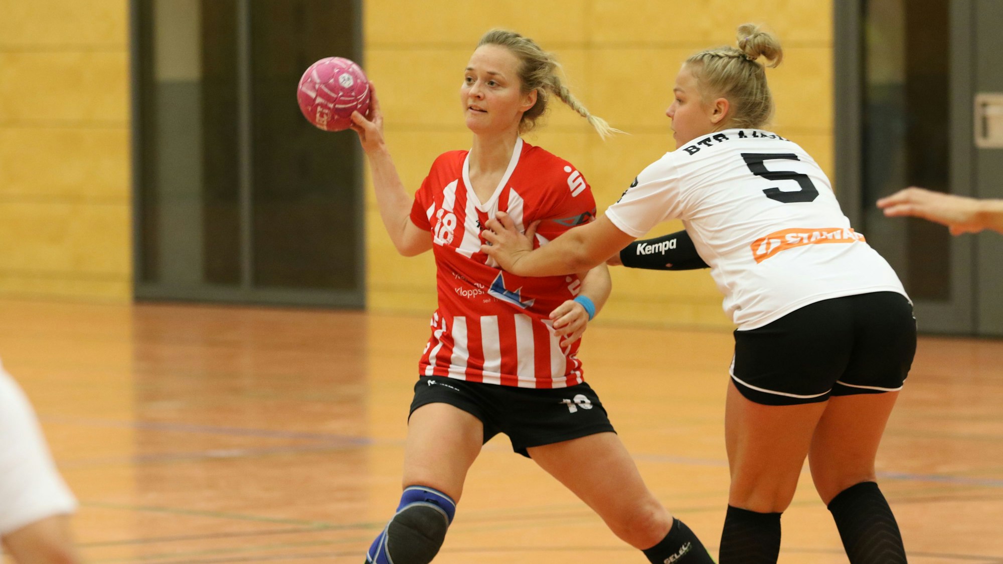 Eine Handballerin spielt einen Pass, eine Gegenspielerin fasst ihr an die Brust.