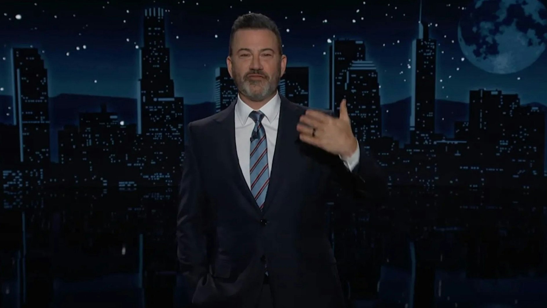 Jimmy Kimmel steht im dunklen Anzug vor der Kulisse seiner Late-Night-Show "Jimmy Kimmel Live!" und gestikuliert mit einer Hand.
