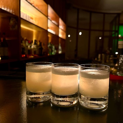 Drei Cocktailgläser mit hellgelber Flüssigkeit stehen nebeneinander auf der Theke.
