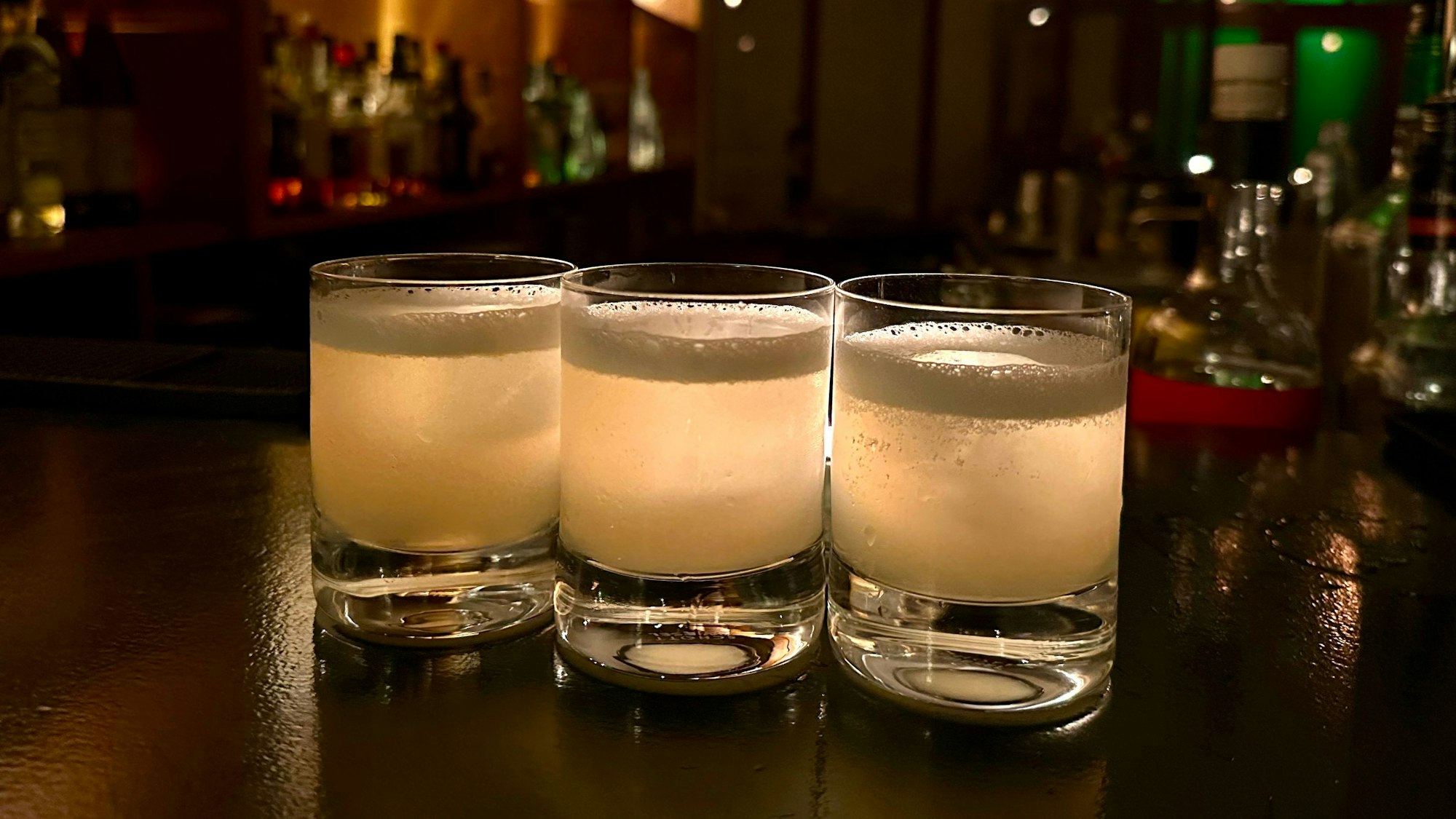 Drei Cocktailgläser mit hellgelber Flüssigkeit stehen nebeneinander auf der Theke.