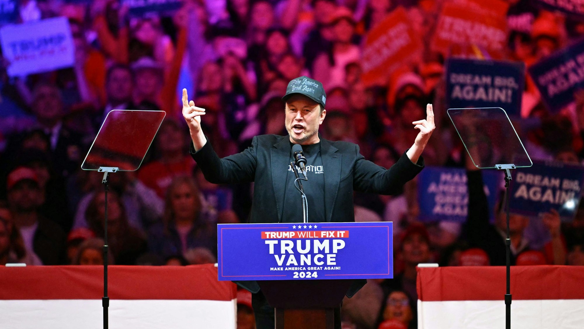 Elon Musk hält eine Rede an einem Pult mit der Aufschrift "Trump, Vance".