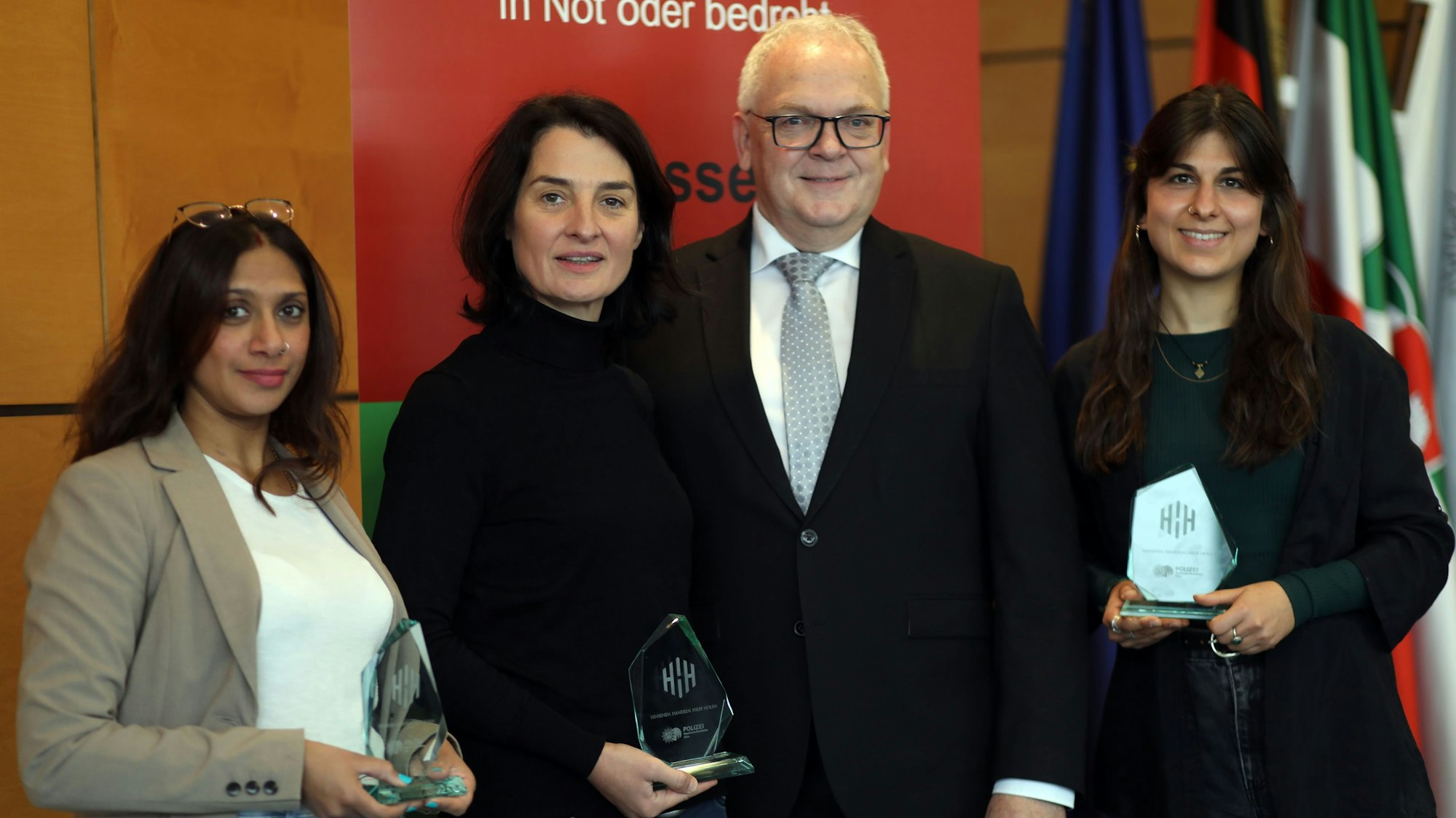 Vier Personen stehen vor einem Banner mit unkenntlicher Schrift. Drei von ihnen halten einen Preis in der Hand.