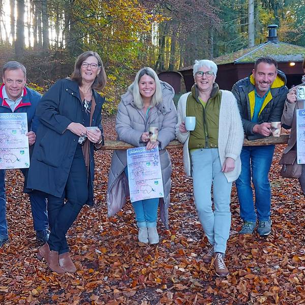 Eine Gruppe von sieben Menschn steht vor einer Grillhütte im Herbstwald.