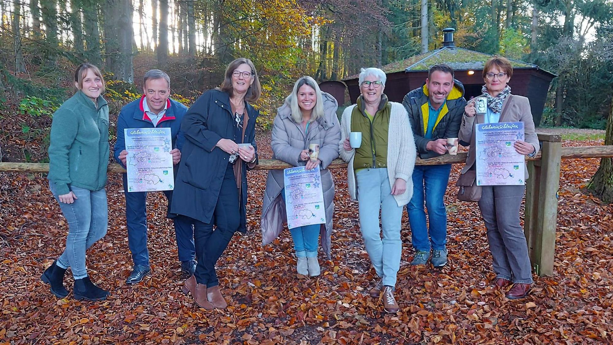 Eine Gruppe von sieben Menschn steht vor einer Grillhütte im Herbstwald.