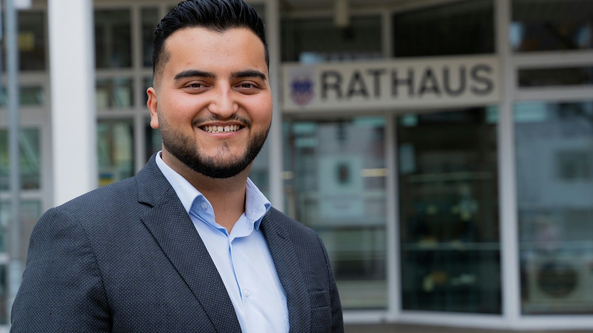 Ein junger Mann in blauem Sakko und blauem Hemd vor dem Eingang zum Rathaus Bad Honnef.