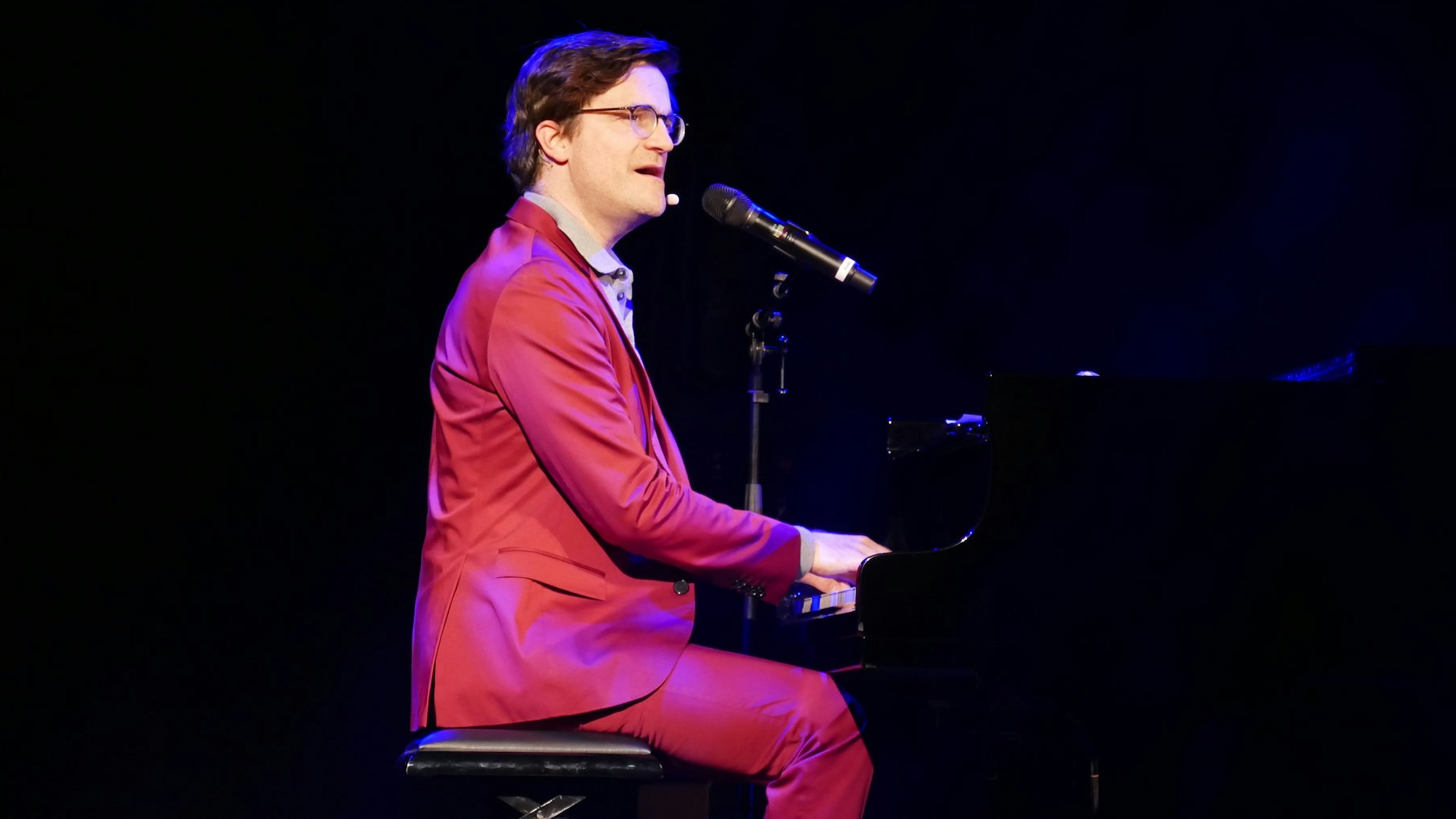 Ein Mann in rotem Anzug sitzt am Klavier.