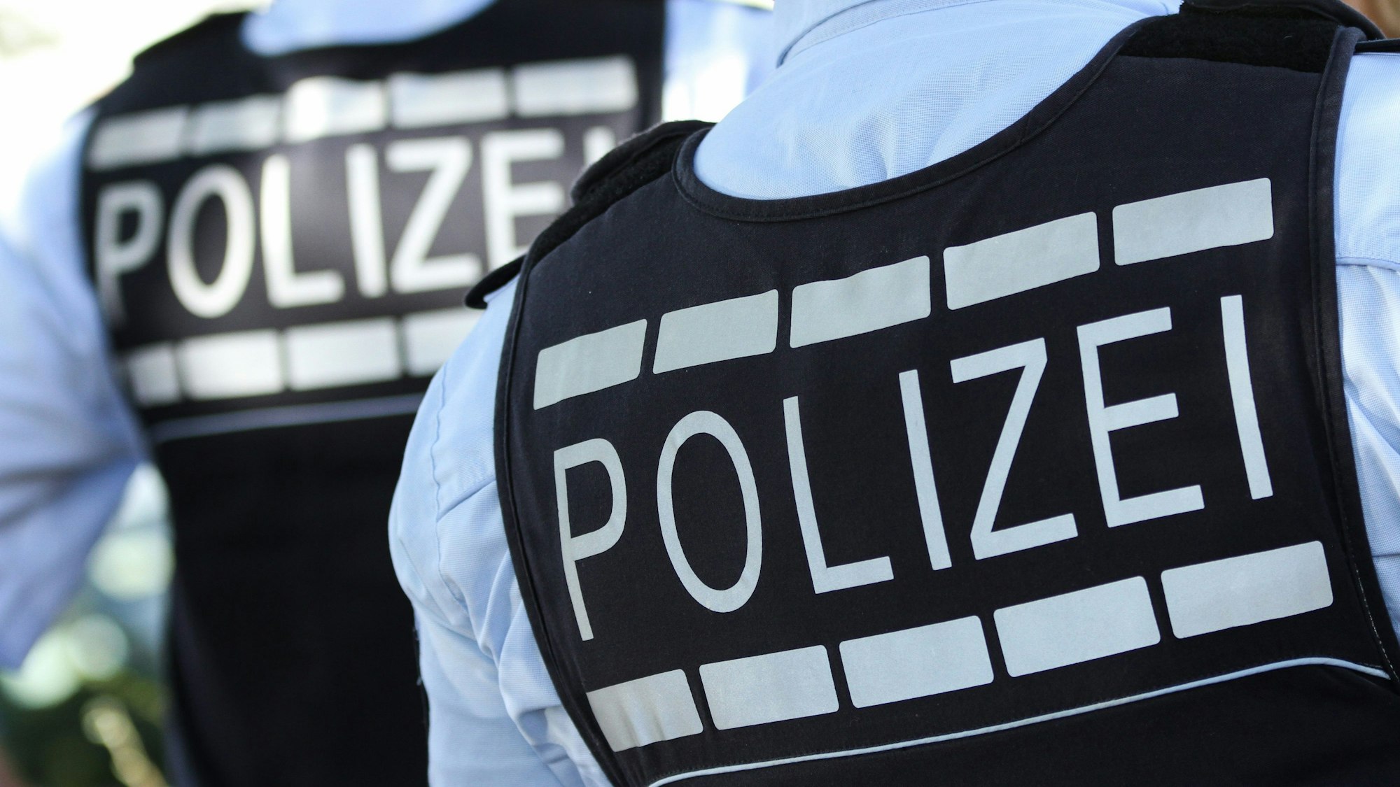 Das Foto zeigt zwei Polizisten von hinten mit der Aufschrift „Polizei“ auf den Schutzwesten.