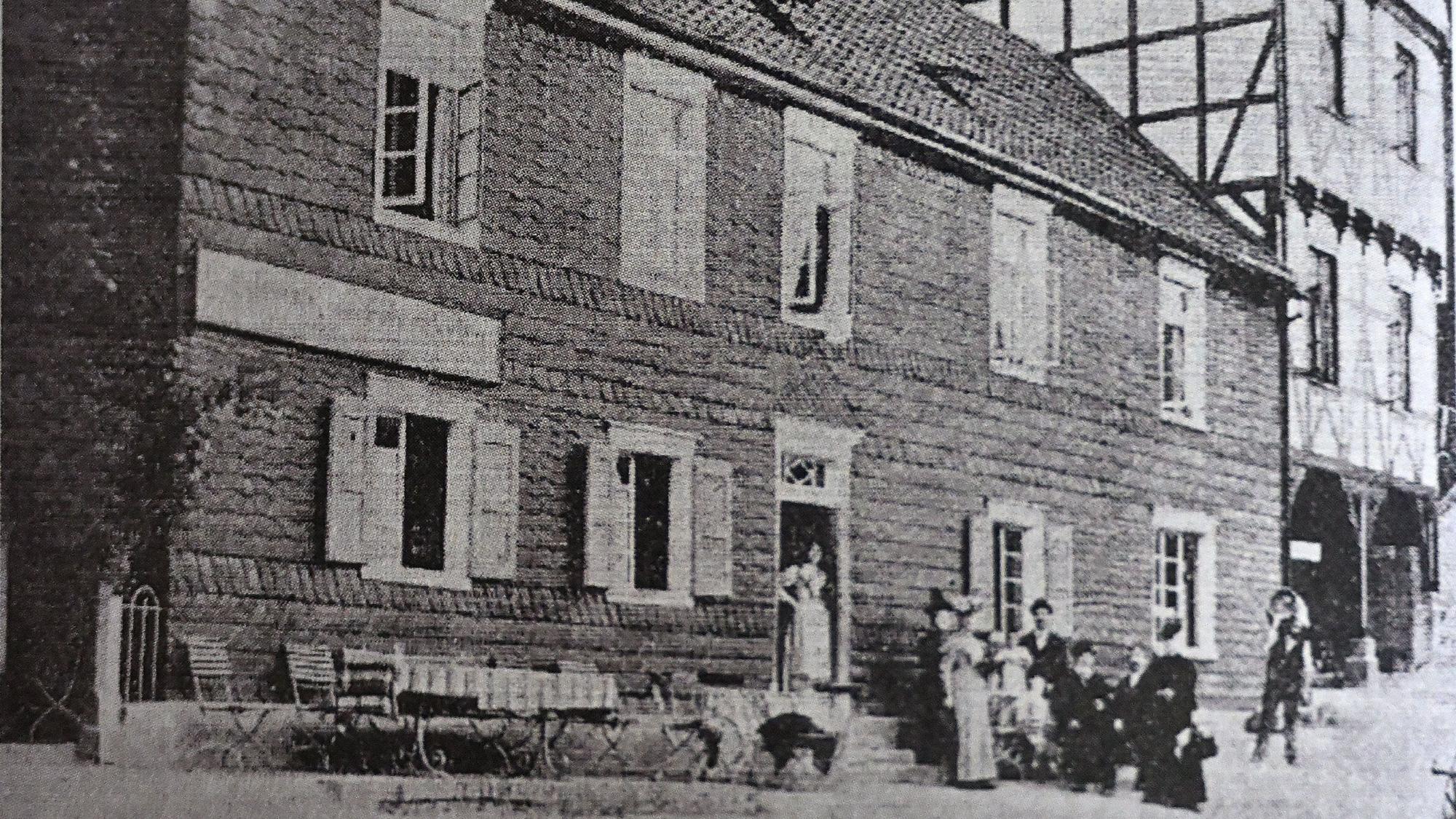 Ein bergisches Lokal, Ende des 19. Jahrhunderts. Davor ein gedeckter Tisch und eine Gruppe von Menschen im Sonntagsstaat