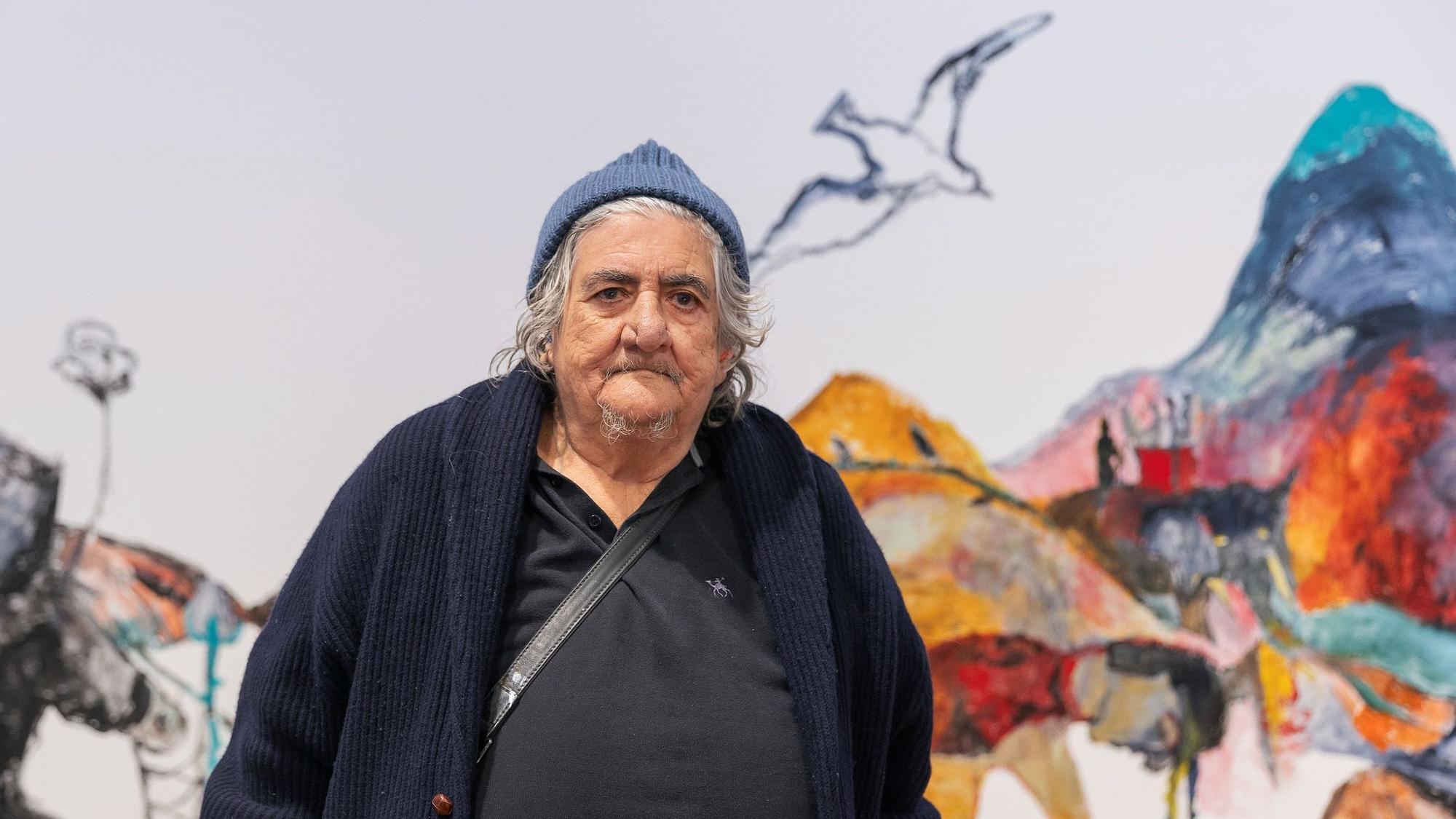 Anna Boghiguian trägt eine Mütze und eine blaue Strickjacke und schaut in die Kamera.