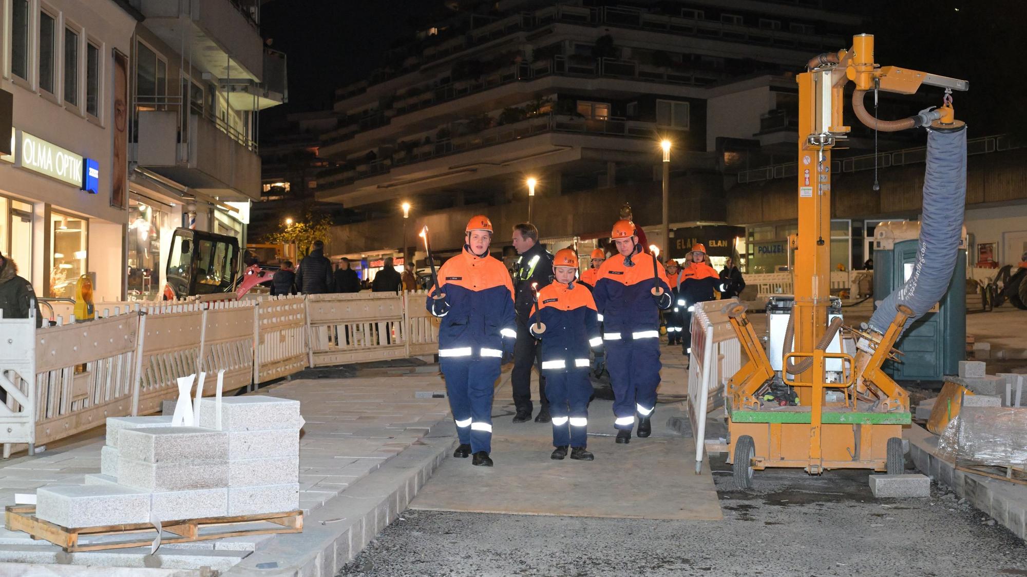 Drei Mitglieder der Jugendfeuerwehr laufen zwischen den Absperrungen entlang.