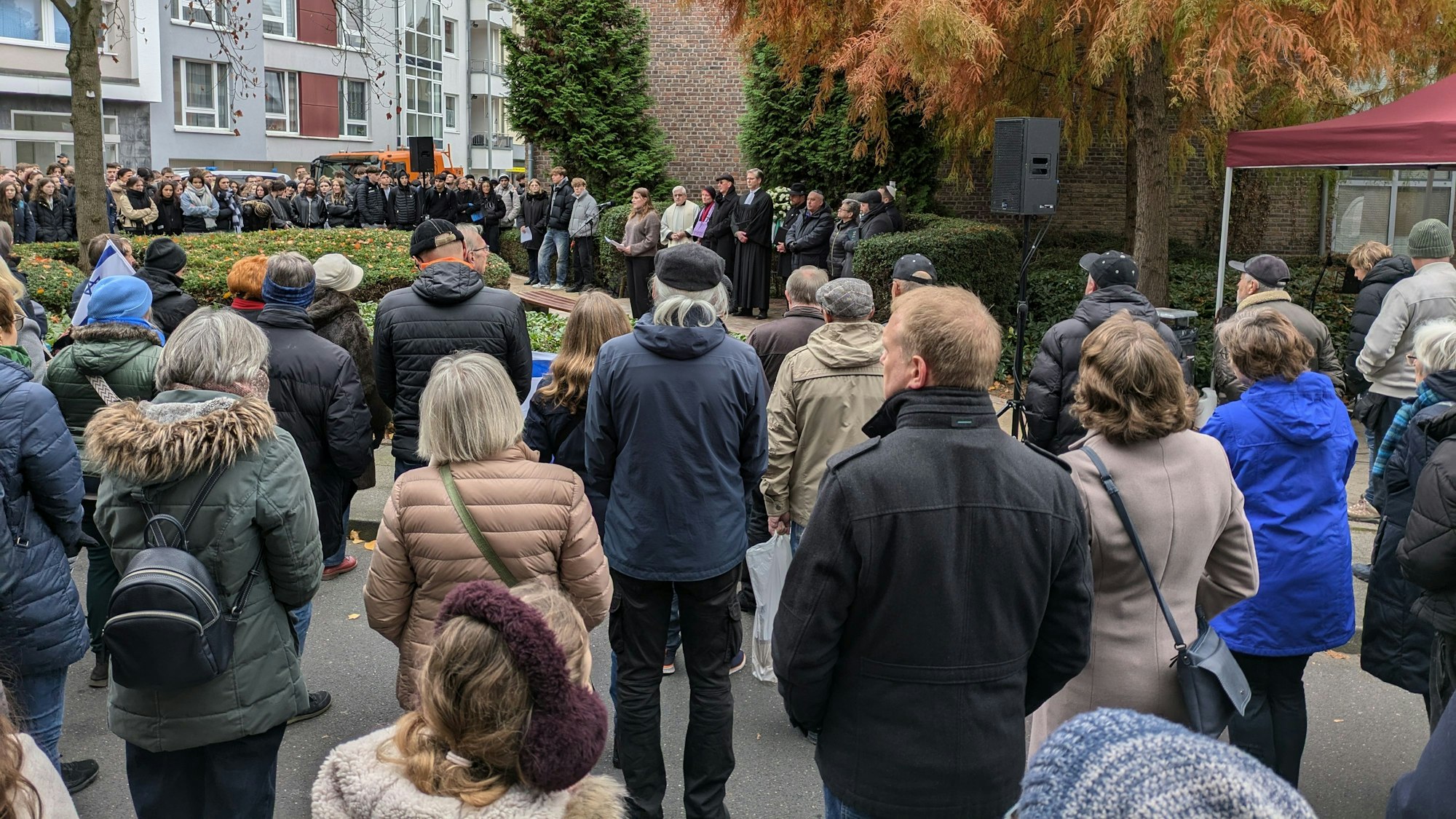 Menschen stehen auf einem Platz und hören einer Rednerin zu.