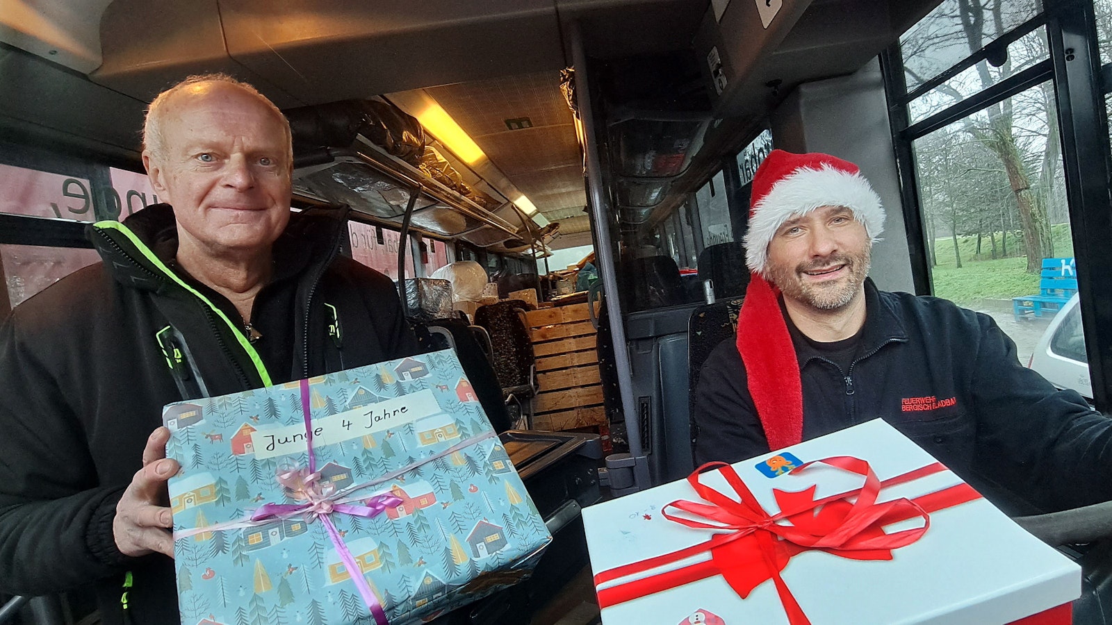 Zwei Männer sitzen mit Wichtelmütze und Paketen in einem Bus.