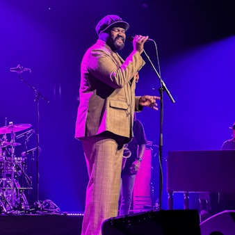 Ein Mann mit einer Mütze steht auf einer Bühne und singt in ein Mikrofon.
