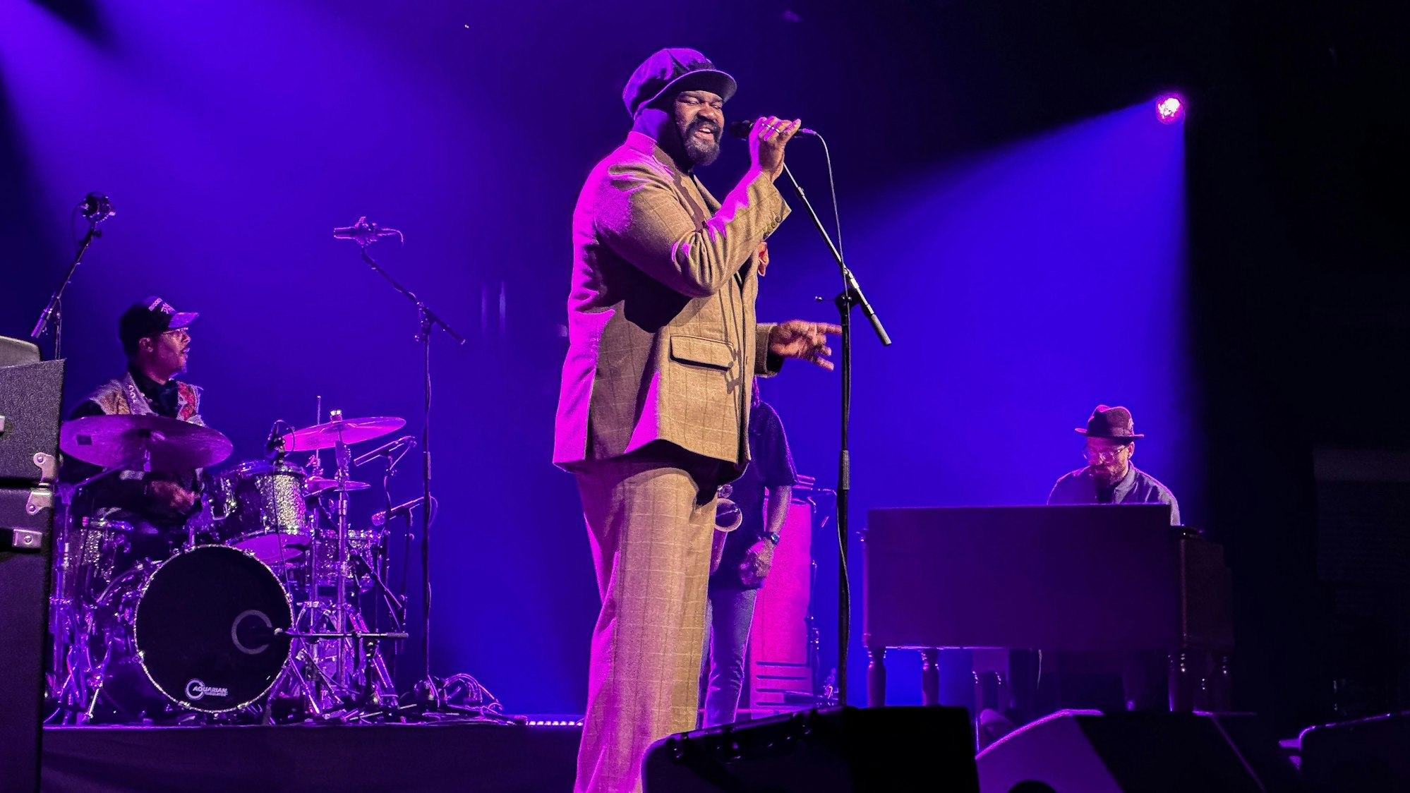Ein Mann mit einer Mütze steht auf einer Bühne und singt in ein Mikrofon.