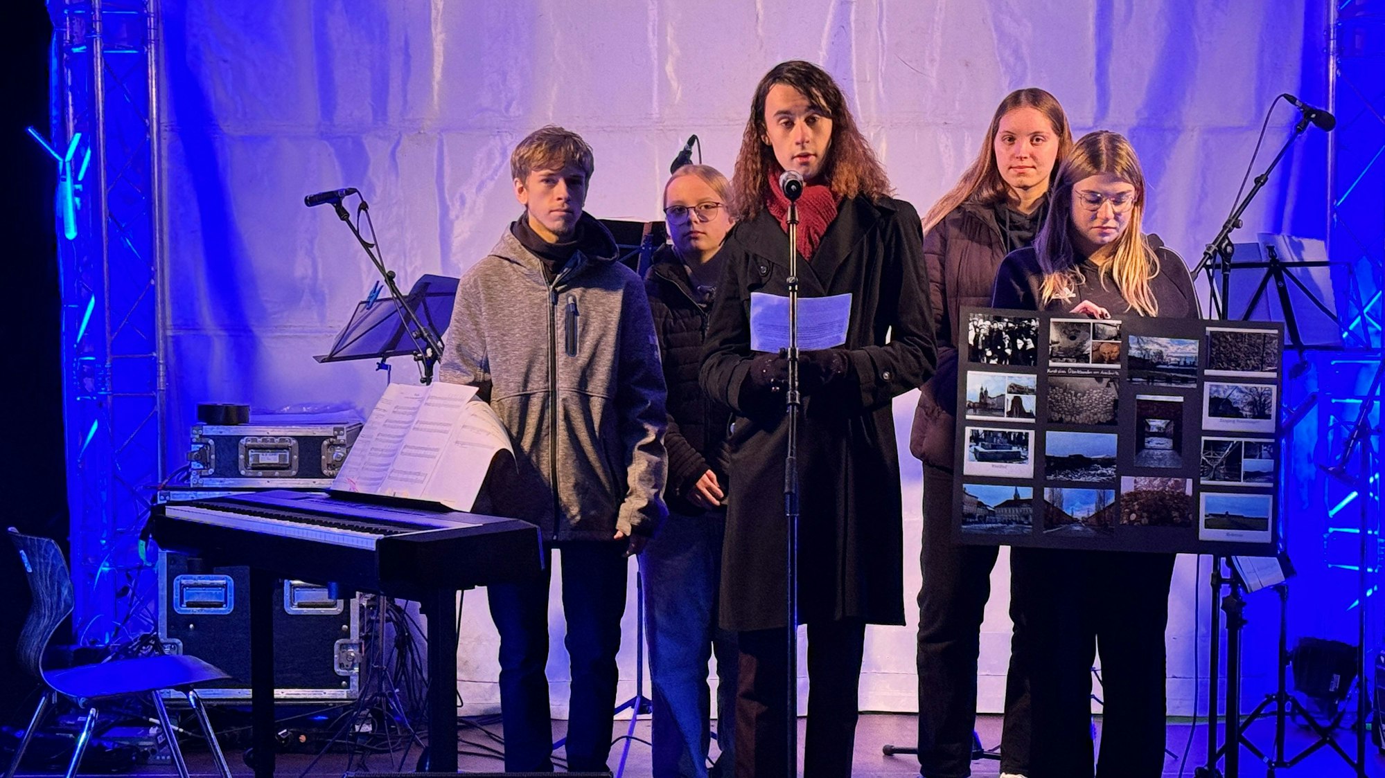 Das Foto zeigt eine Gruppe von Schülerinnen und Schülern auf einer Bühne. Eine Schülerin hält eine Collage von Bildern in den Händen.