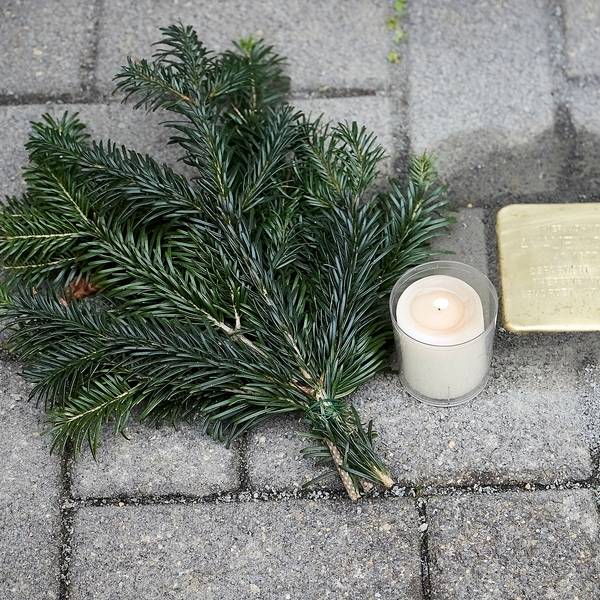 Ein neu verlegter Stolperstein, neben dem eine Kerze und ein Tannenzweig liegt.