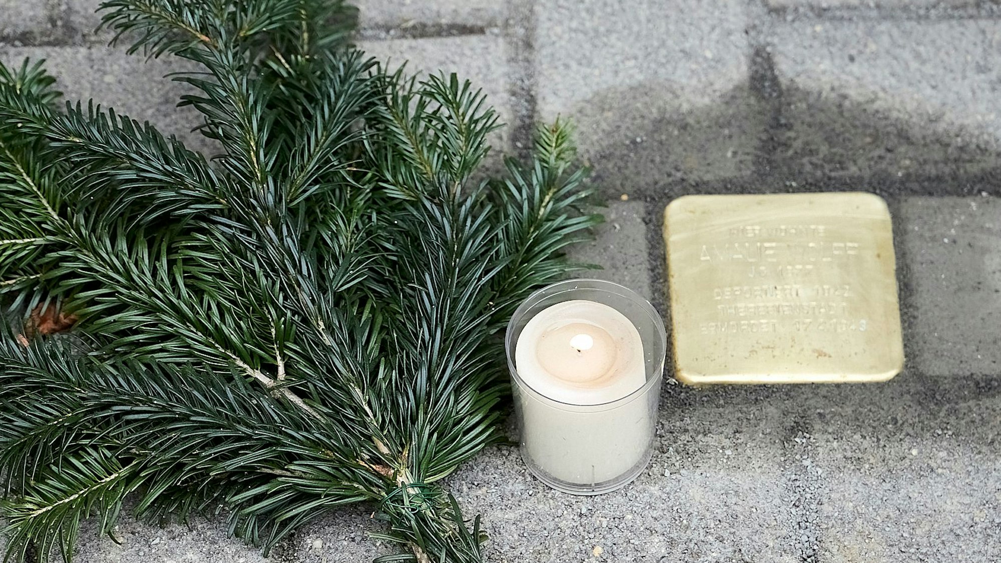 Ein neu verlegter Stolperstein, neben dem eine Kerze und ein Tannenzweig liegt.