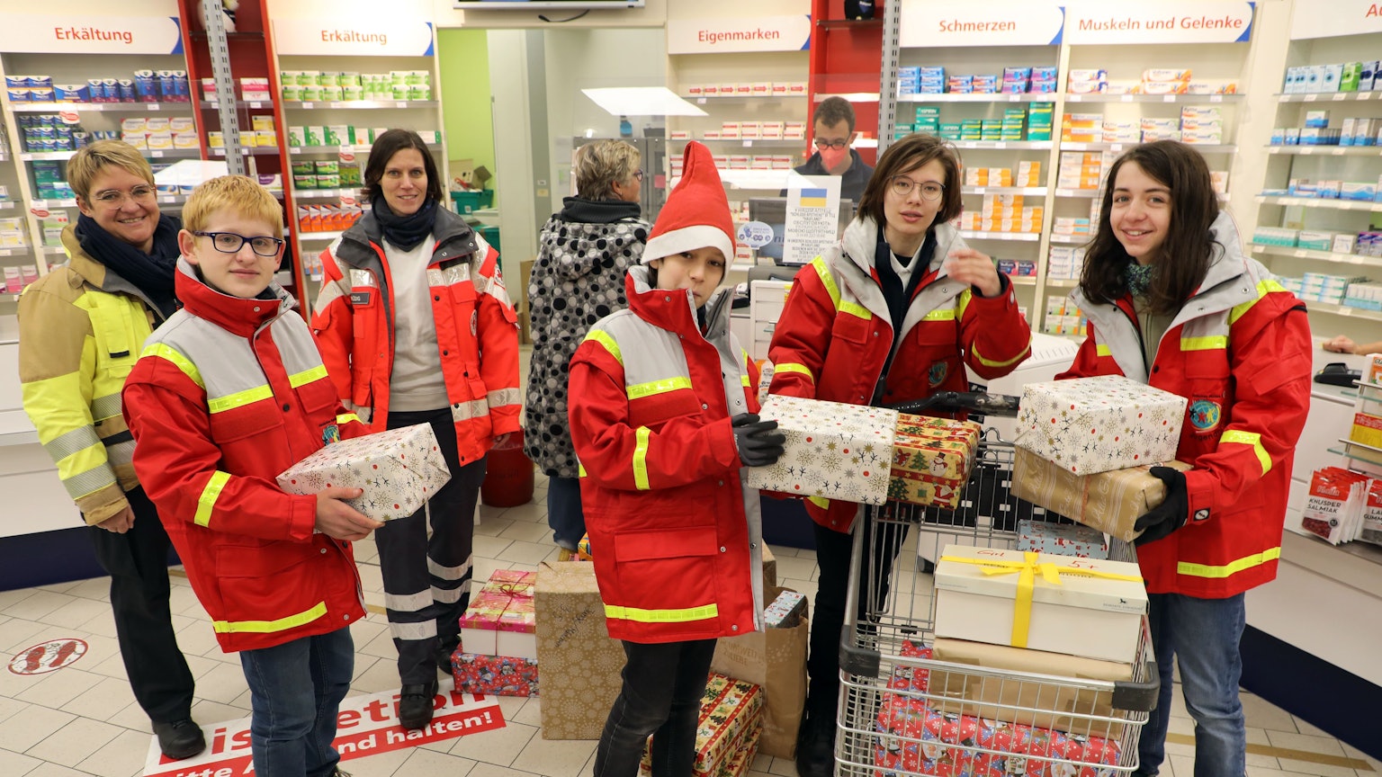 Jugendrotkreuzler und Mitarbeiterinnen von DRK und Feuerwehr holen gespendete Pakete für die Wichtelaktion 2022 in einer Apotheke ab.