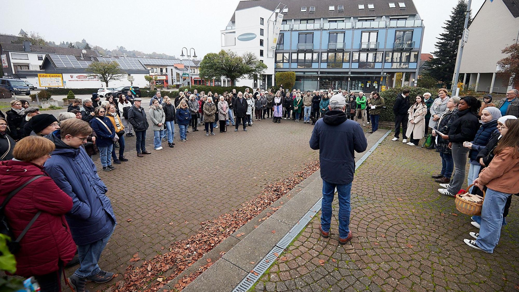 Auf dem Brunnenplatz stehen viele Menschen im Kreis und hören einem Mann zu, der in der Mitte steht.