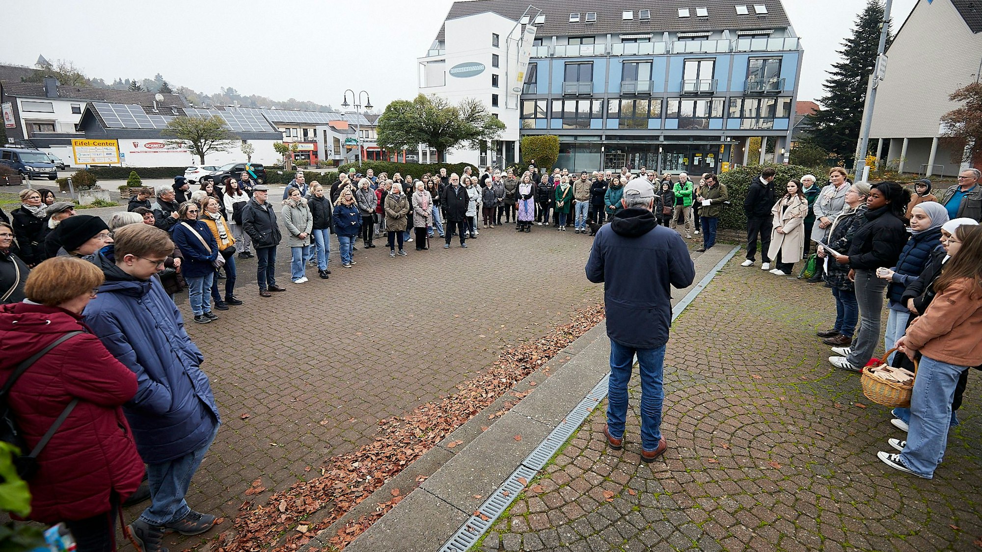 Auf dem Brunnenplatz stehen viele Menschen im Kreis und hören einem Mann zu, der in der Mitte steht.