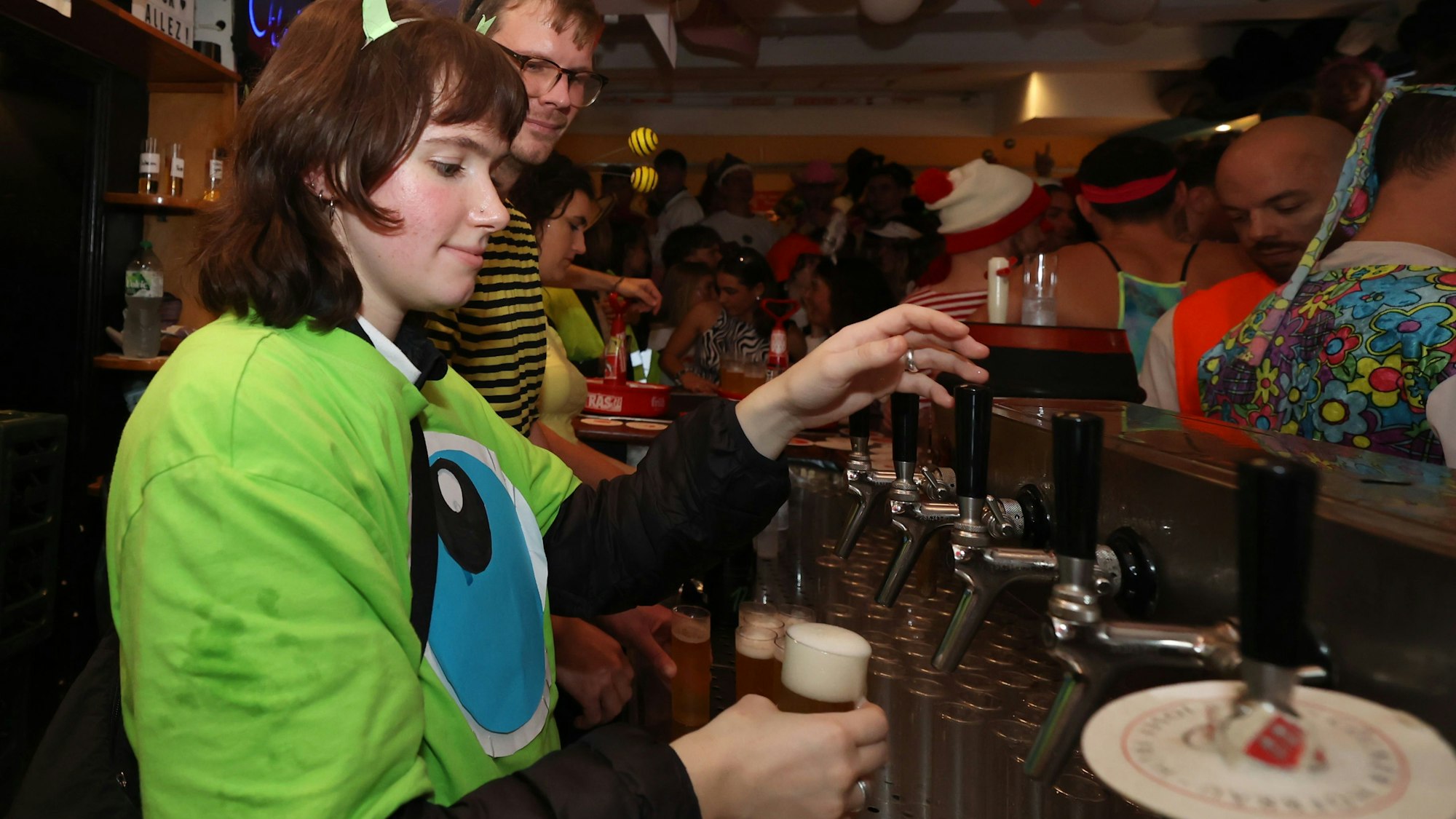 Frau in einem grünen Monster-Kostüm zapft Bier.