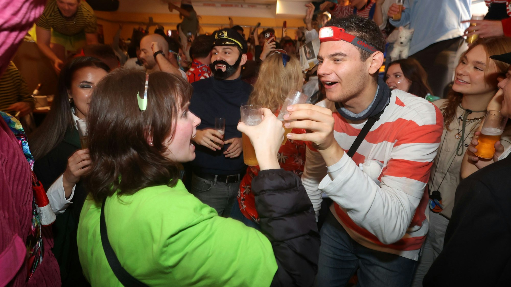 Zwei verkleidete Menschen stoßen in einer Menschenmenge mit einem Bier an.