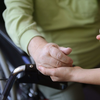 Eine junge Frau hält die Hände eines alten Mannes.
