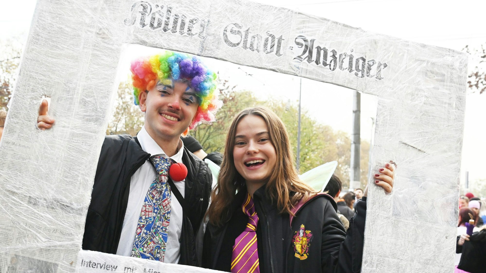 Zwei Personen in Clown-Kostüm und Gryffindor-Robe halten einen überdimensionierten „Kölner Stadt-Anzeiger“ als Bilder-Rahmen fest.