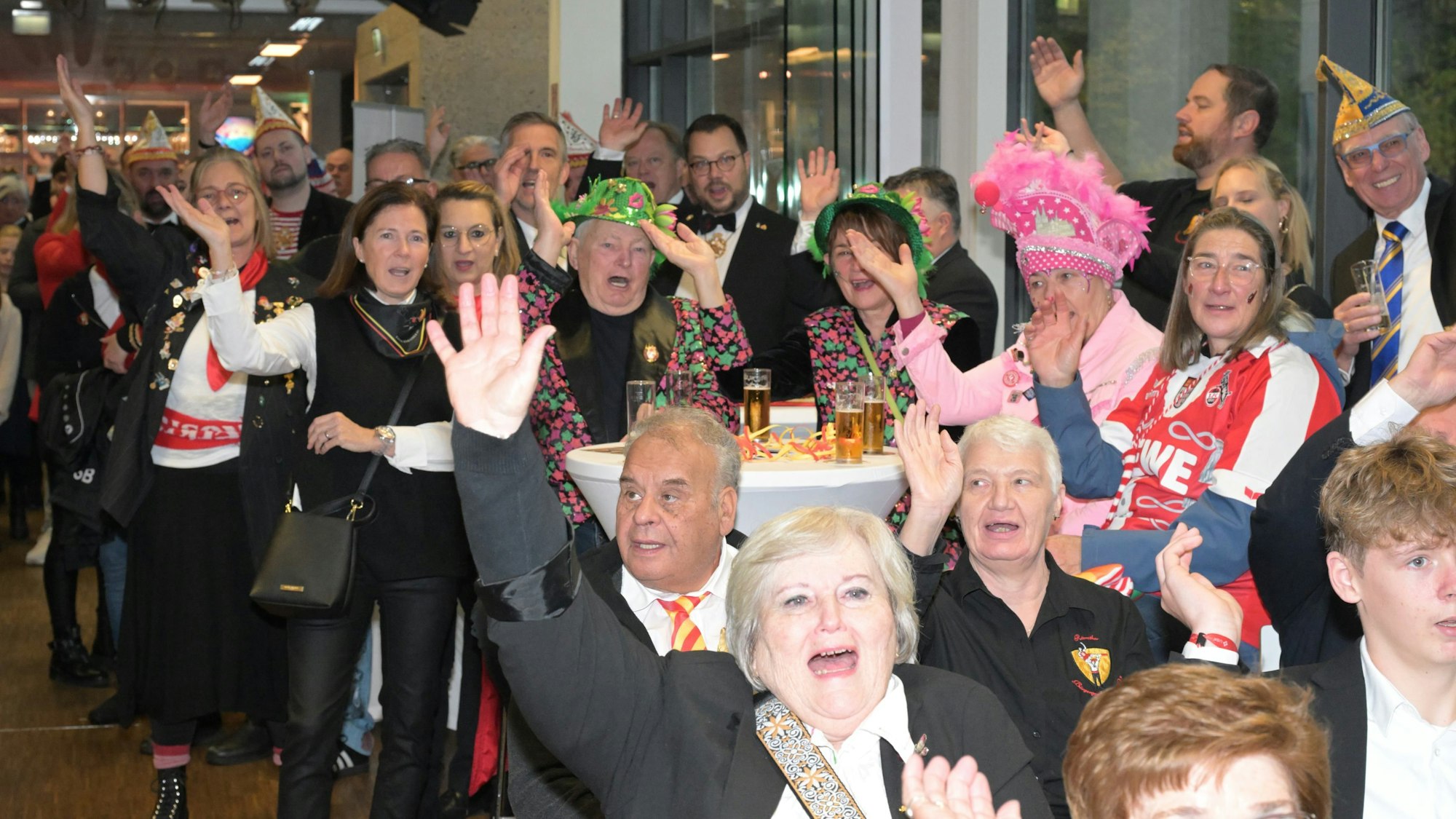 Sitzend an den Tischen und stehend heben die kostümierten Karnevalisten die Hände, um Alaaf zu rufen.