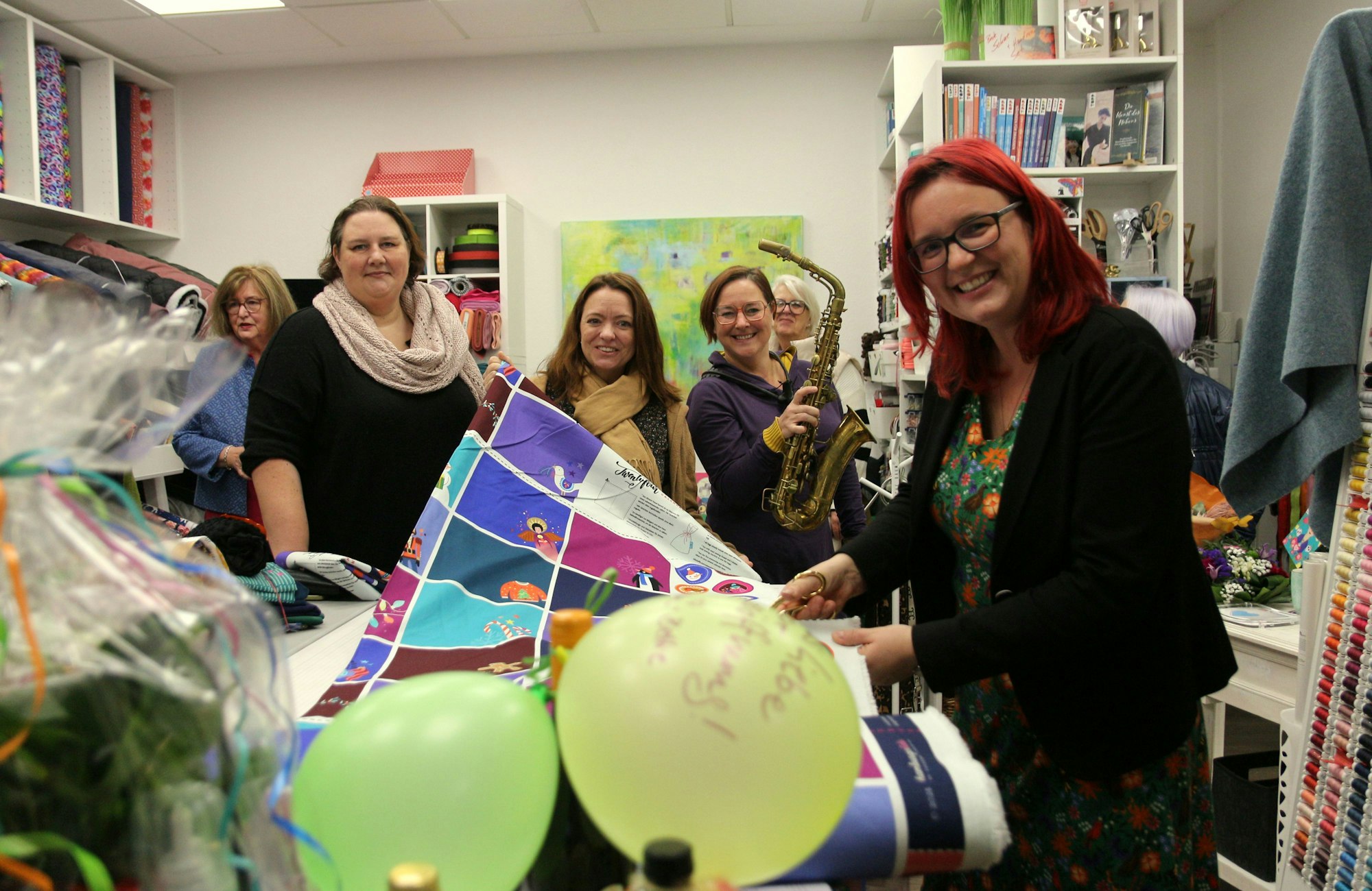 Frauen lächeln in die Kamera, auf einem Tisch vor ihnen liegen Luftballons und eine Stoffbahn.