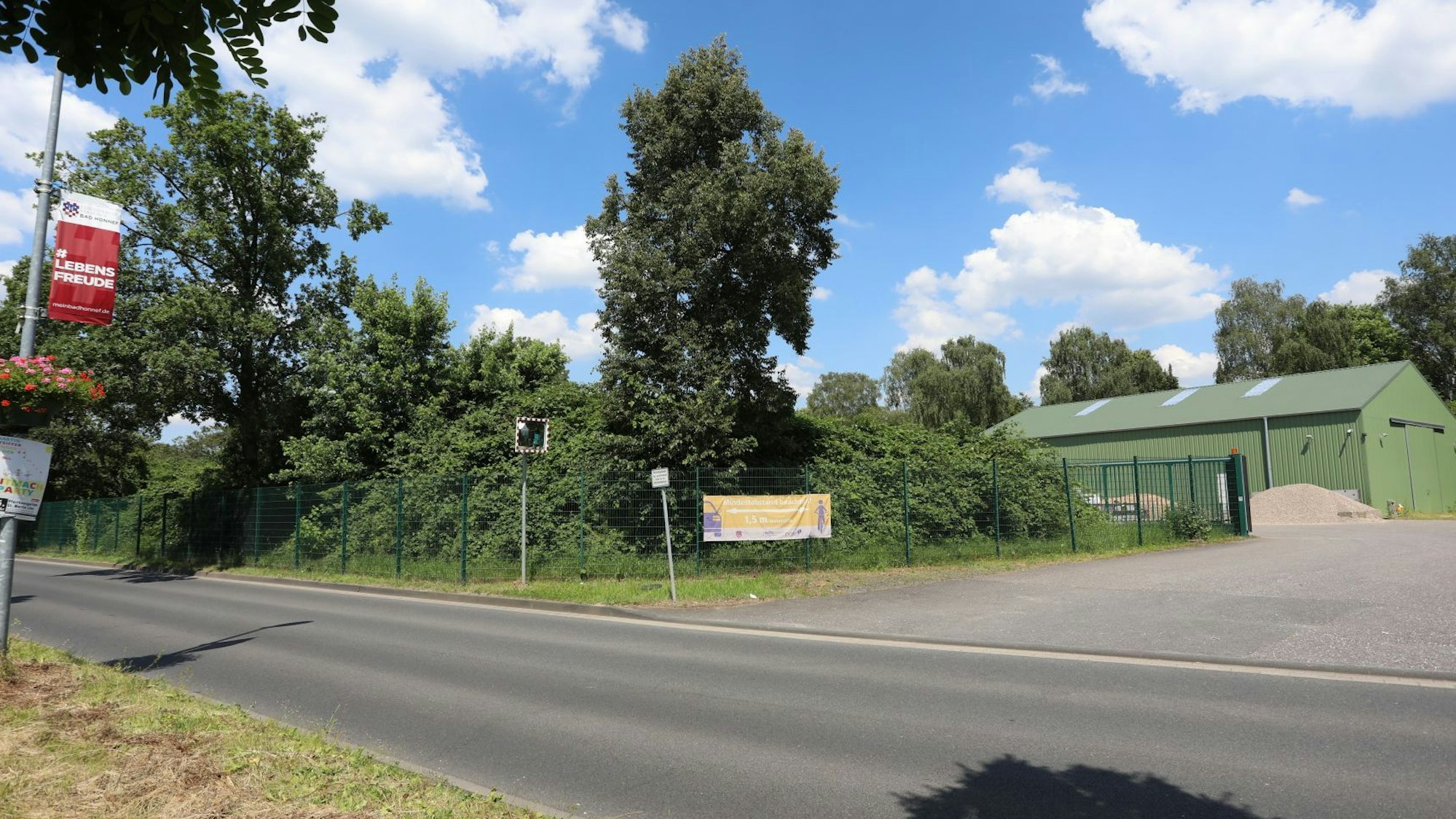 Eine Straße im Vordergrund, auf der anderen Straßenseite steht eine grüne Lagerhalle.