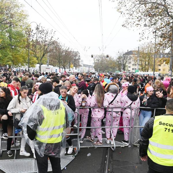 Feiernde stehen vor einem Absperrgitter mit Sicherheitskräften.