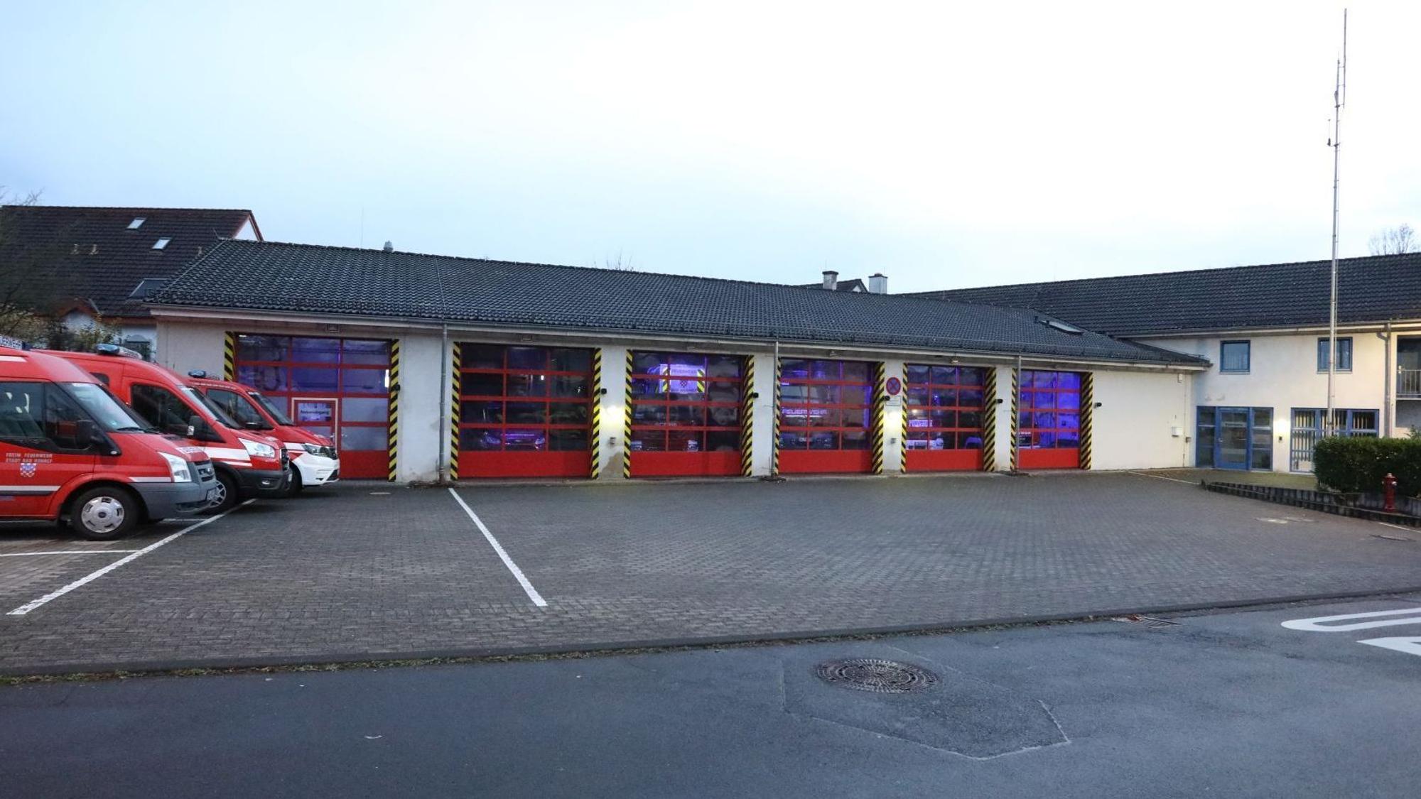 Eine Feuerwache mit roten Rolltoren, links stehen drei Feuerwehrfahrzeuge im Freien.