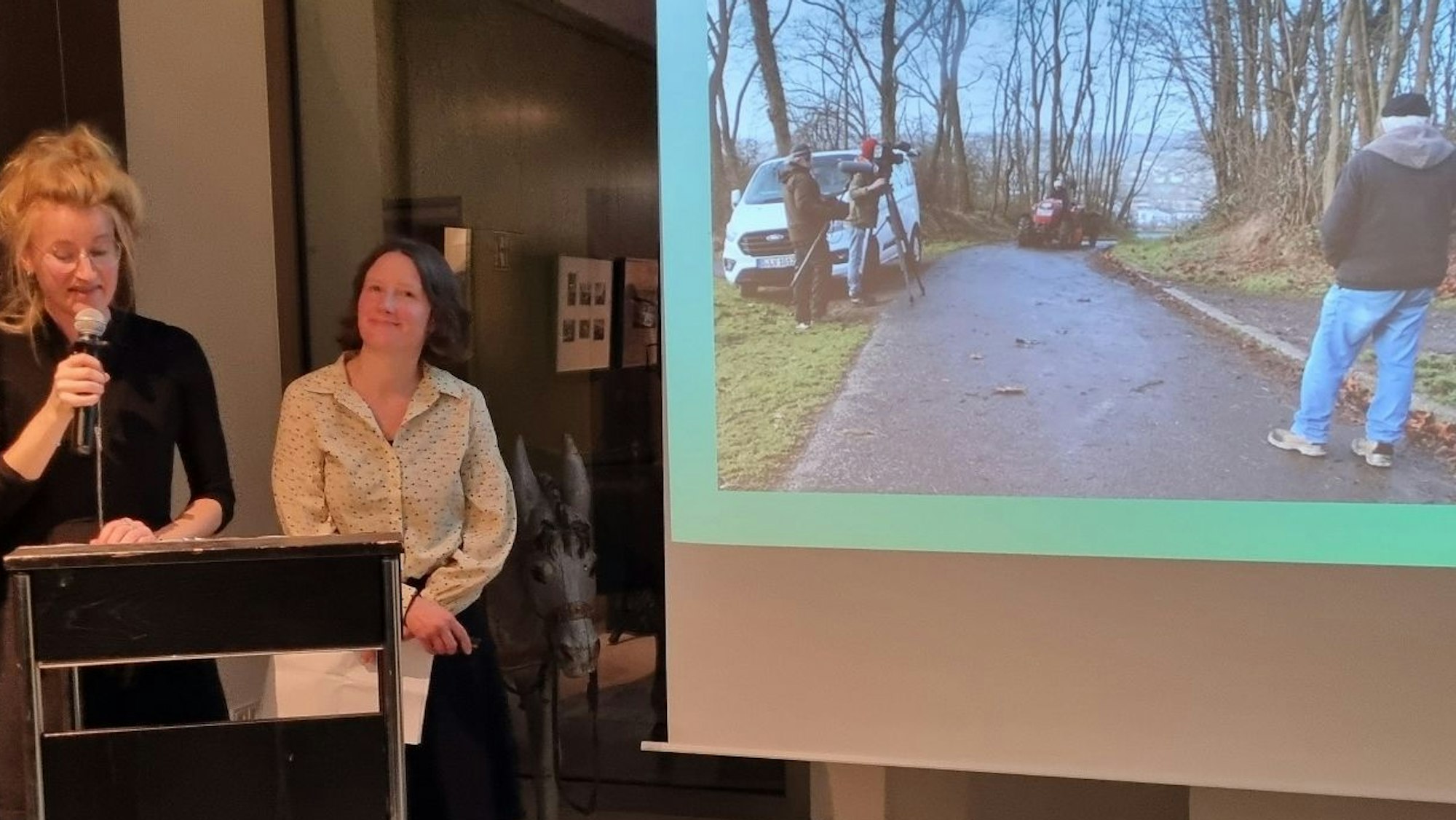 Zwei Frauen neben einer Leinwand, auf der Dreharbeiten für einen Film gezet werden.