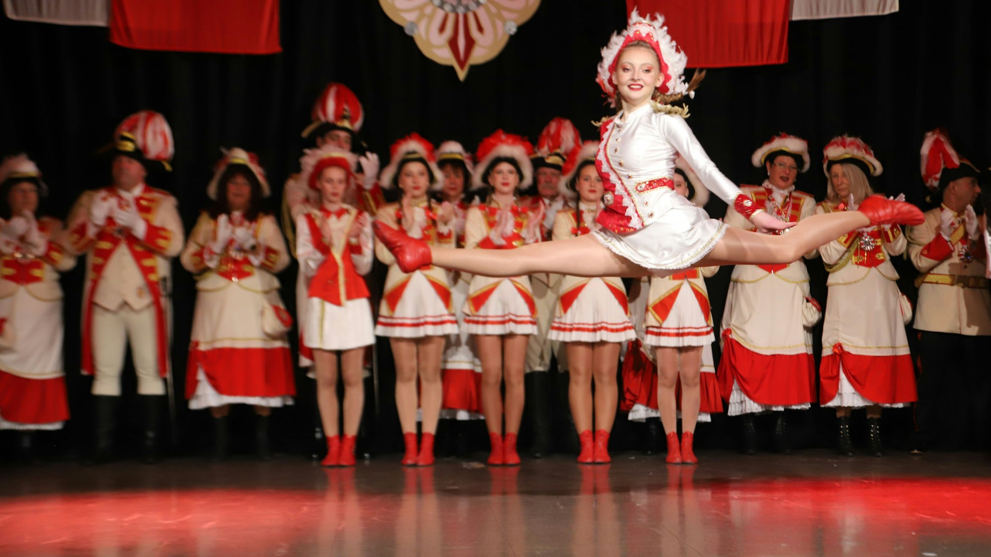 Ein Tanzmariechen springt vor einer Garde mit gestreckten Beinen in die Höhe.