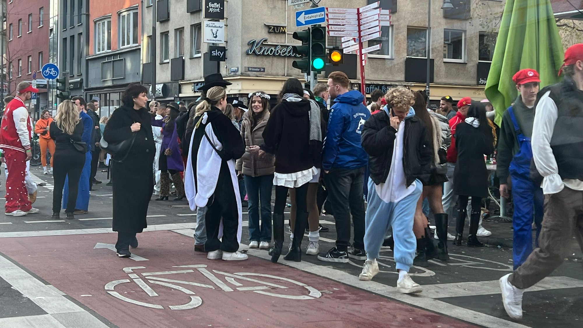 An der Aachener Straße im Belgischen Viertel herrscht großer Andrang vor den Kneipen und Kiosks. Die Jecken stehen in großen Gruppen auf der Straße, man hört wie Glasflaschen zerbrechen, die Autos stauen sich.