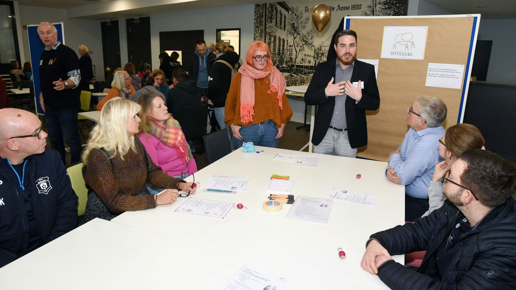 Menschen sitzen und stehen um einen Tisch und diskutieren.