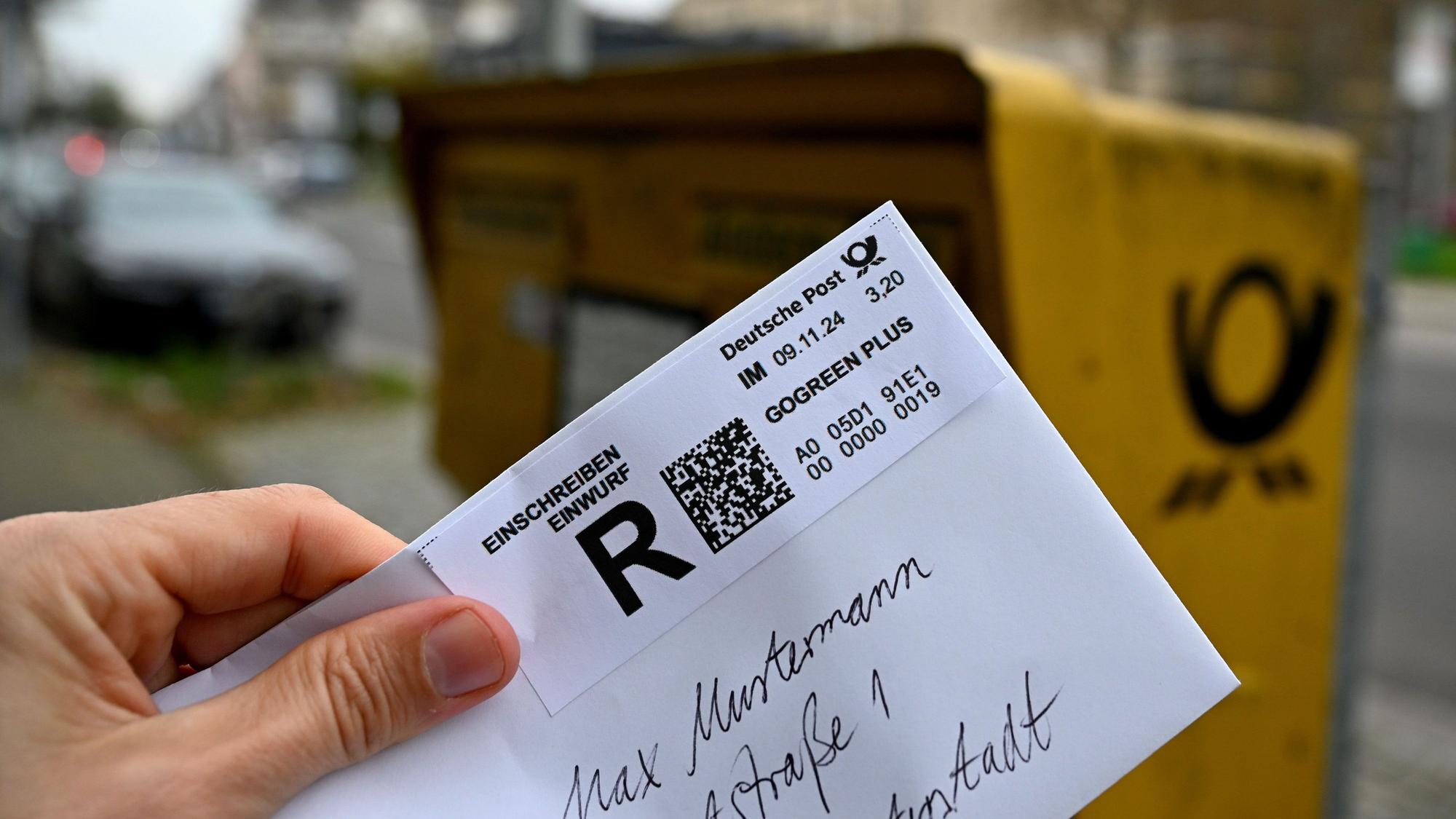 09.11.2024, Nordrhein-Westfalen, Düsseldorf: ILLUSTRATION - Ein Mann hält ein sogenanntes Einwurf-Einschreiben vor einen Briefkasten (gestellte Szene).
