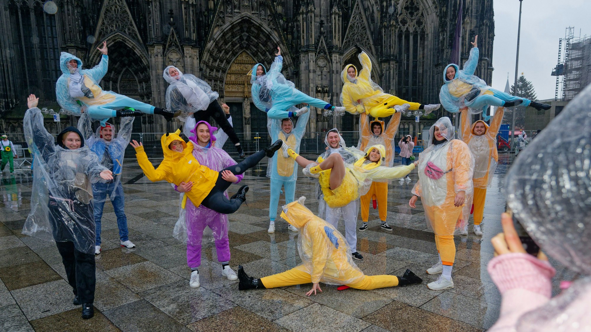 11.11.2024, Nordrhein-Westfalen, Köln: Eine karnevalistische Tanzgruppe aus Belgien posiert bei leichten Nieselregen vor dem Dom für ein Foto.