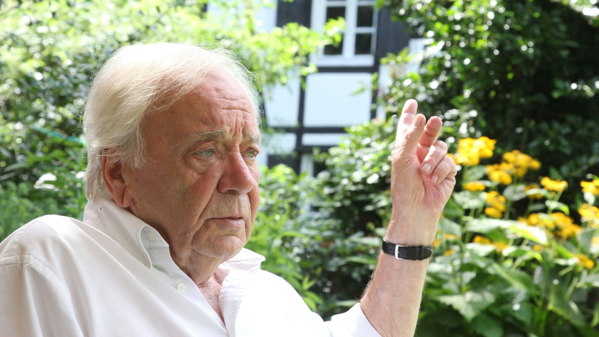 Ein älterer Mann sitzt in einem Garten und diskutiert.