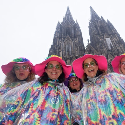Karnevalistinnen posieren im Regen mit großen Hüten vor dem Dom für ein Foto. (Archivbild)