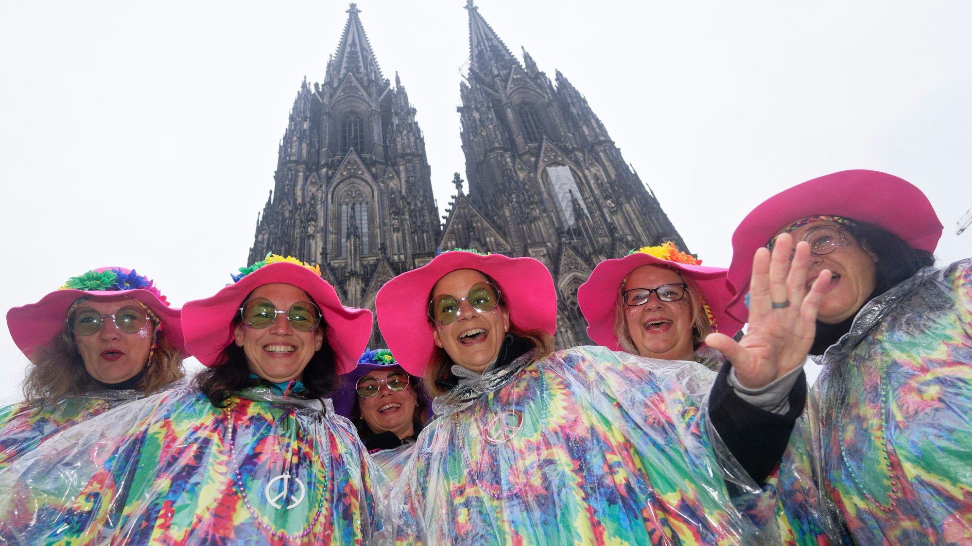Karnevalistinnen posieren im Regen mit großen Hüten vor dem Dom für ein Foto. (Archivbild)