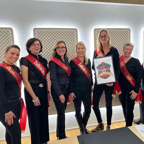 Das Bild zeigt die acht Gründungsmitglieder. Sie alle sind in Schwarz gekleidet und haben rote Schärpen an.