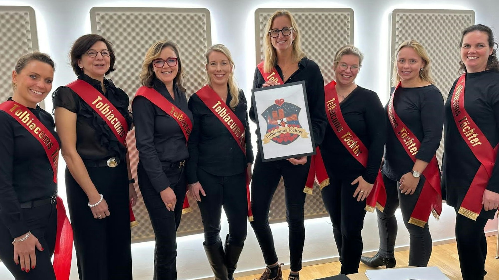 Das Bild zeigt die acht Gründungsmitglieder. Sie alle sind in Schwarz gekleidet und haben rote Schärpen an.