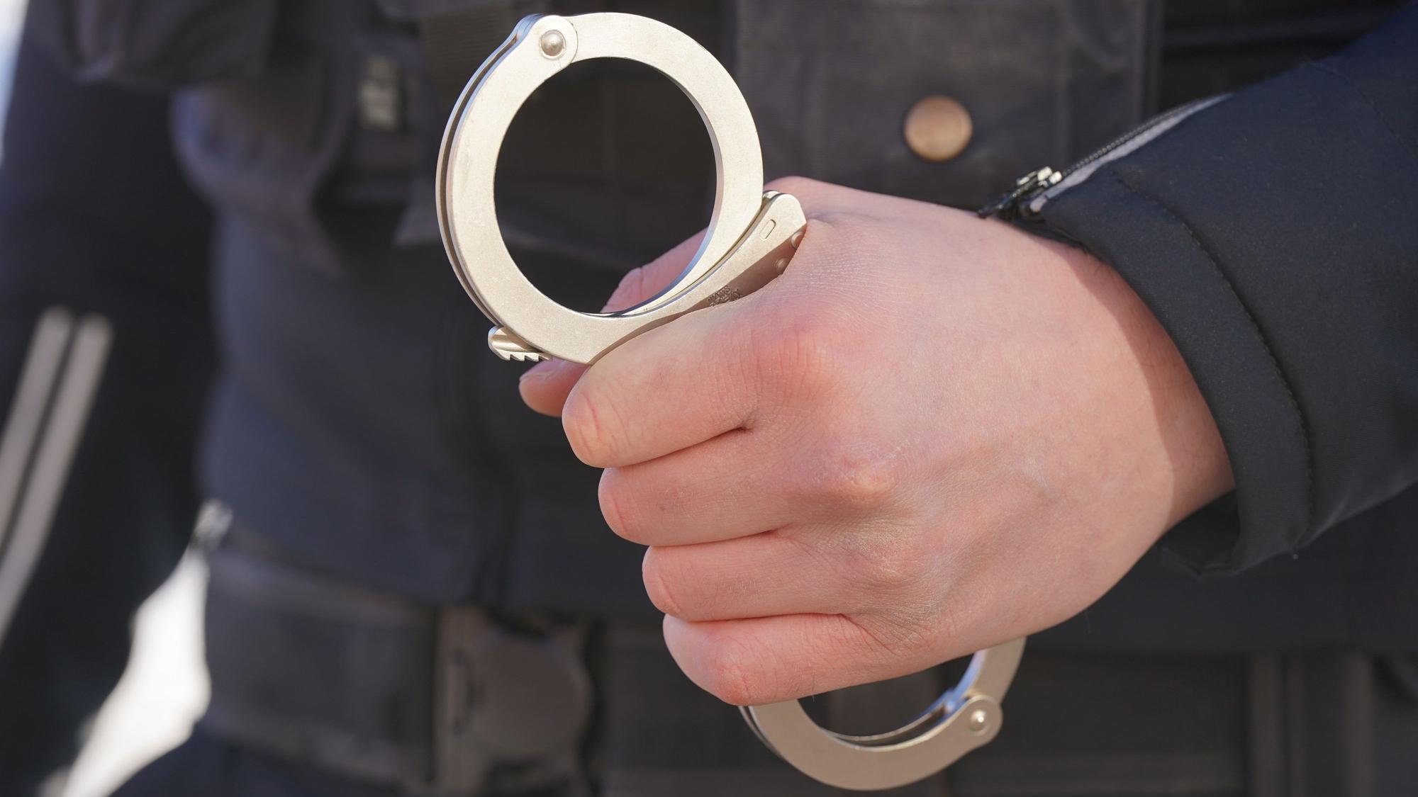Auf dem Foto ist ein Polizist zu sehen, der Handschellen in der Hand hält.